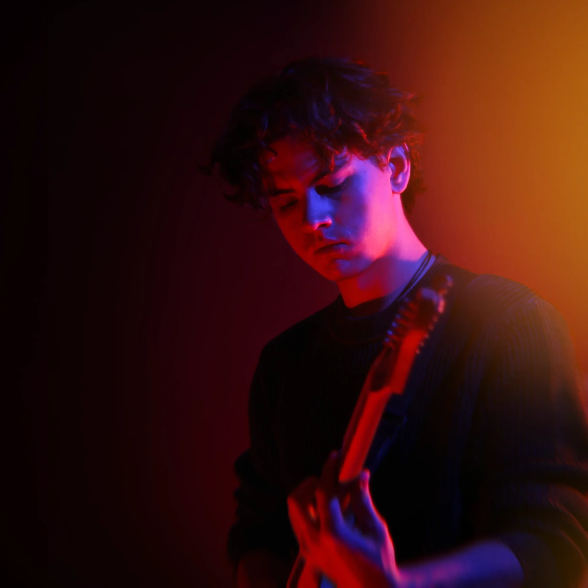 Picture of Defy Tracks Founder Ben Davidson, on a dark background with colorful lighting while he plays guitar.